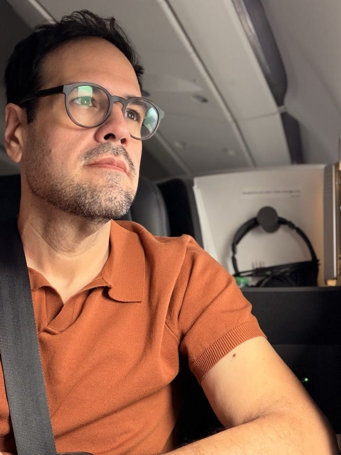 Marcio in an airplane seat with his seatbelt on, April 2026